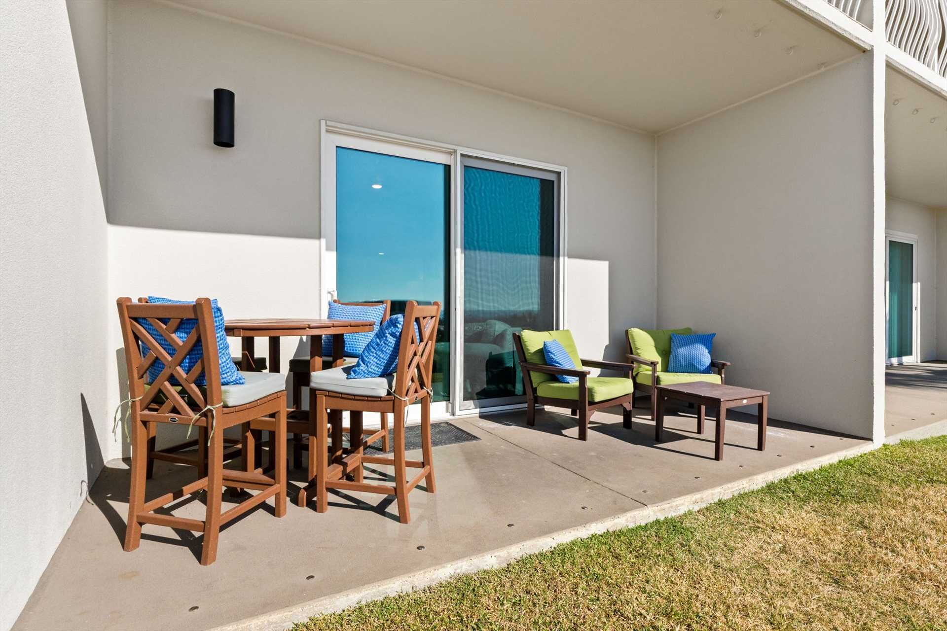 Une terrasse extérieure avec des chaises et une table en bois, une porte-fenêtre coulissante et une petite table avec un coussin.