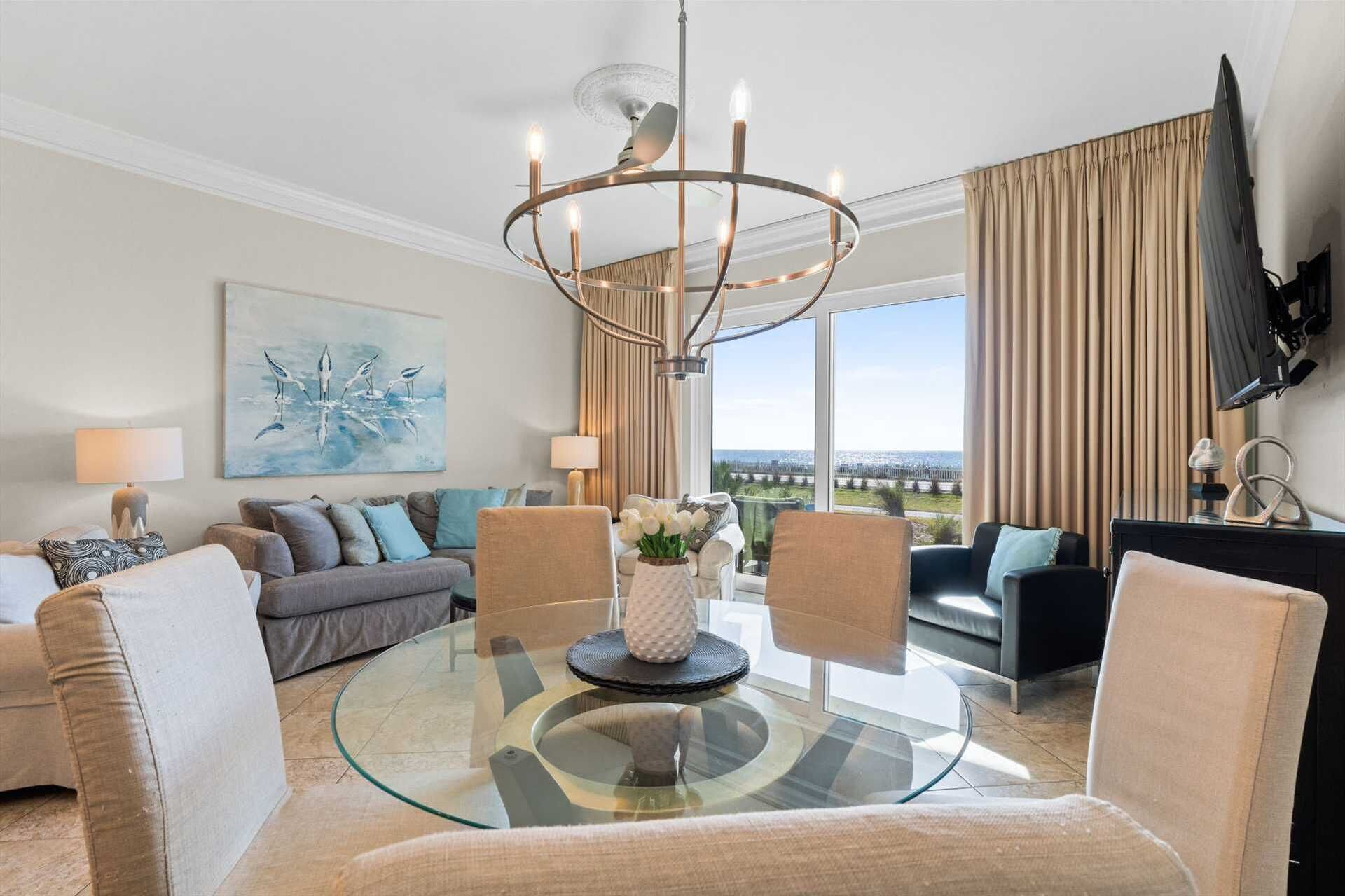 A modern living room with a glass coffee table, comfortable seating, a large painting, and a view of the outdoors.