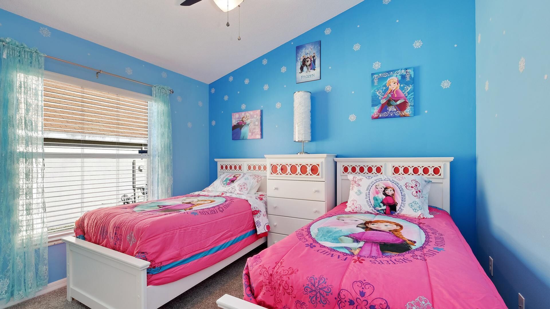 Une chambre avec deux lits, une fenêtre avec des stores et un ventilateur de plafond.
