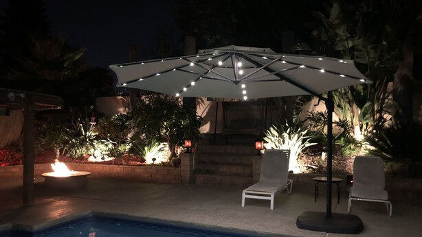 A poolside area with a white umbrella, two lounge chairs, and a fire feature.