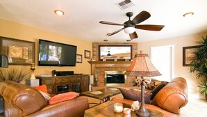 A living room with leather sofas, a fireplace, a television, and a ceiling fan.