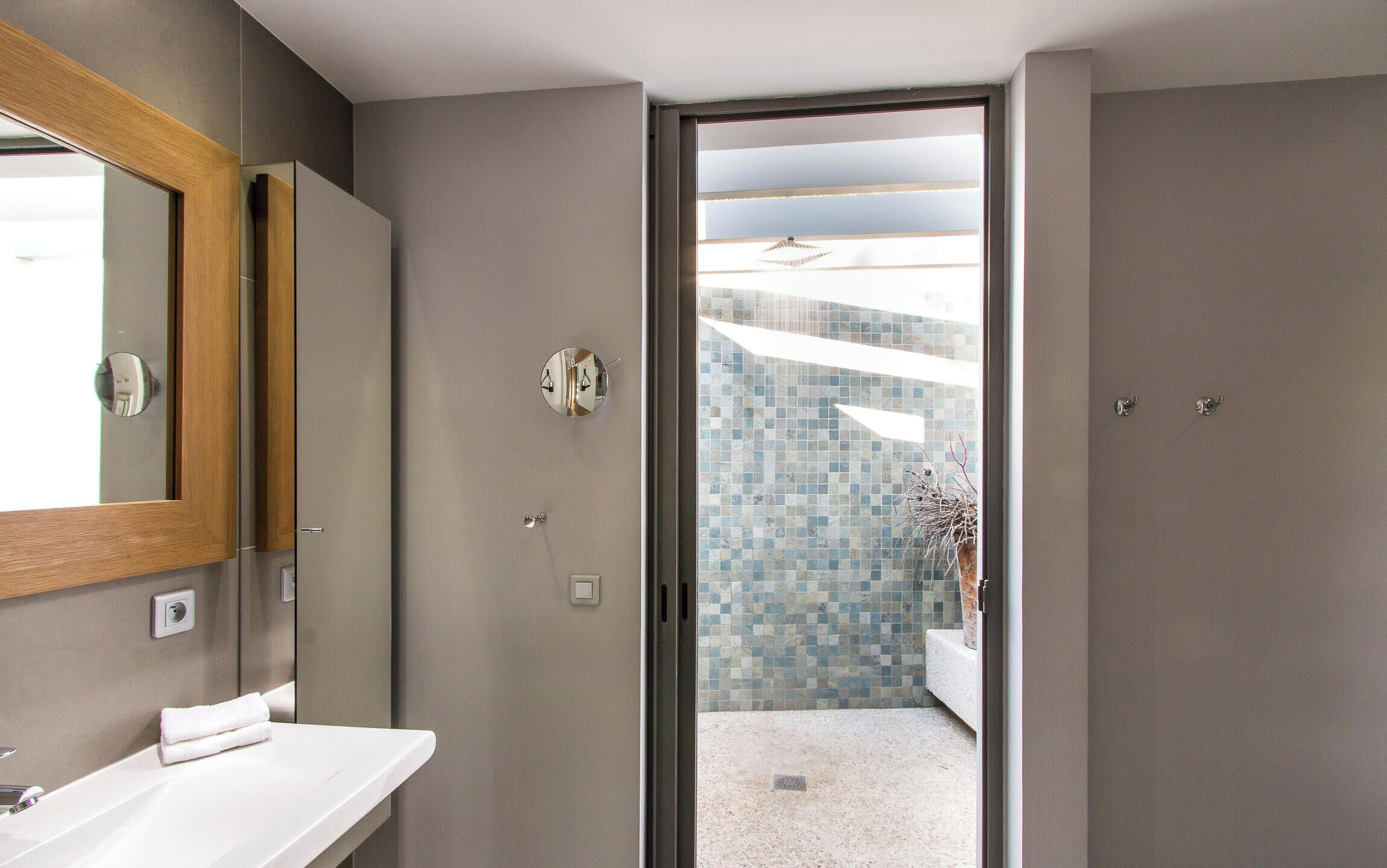 A modern bathroom with a white vanity, a large mirror, and a shower area visible through an open door.