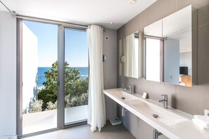 Een moderne badkamer met een groot raam, een witte wastafel en een spiegel.