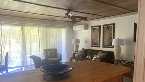 A room with a wooden dining table, a ceiling fan, a sofa with patterned cushions, and framed artwork on the wall.