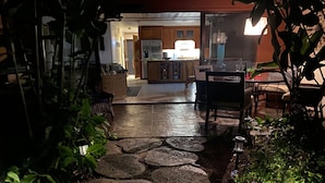 A stone pathway leading to a dining area with a table and chairs, surrounded by greenery.
