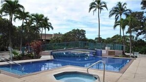 A swimming pool with a hot tub, surrounded by palm trees and a fence.