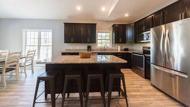 A modern kitchen with dark cabinets, a stainless steel refrigerator, and a central island with bar stools. - Built in 2017 - 4 BR/3 BA Lakeview in Grand Rivers - The Only City on Both Lakes (Grand Rivers)