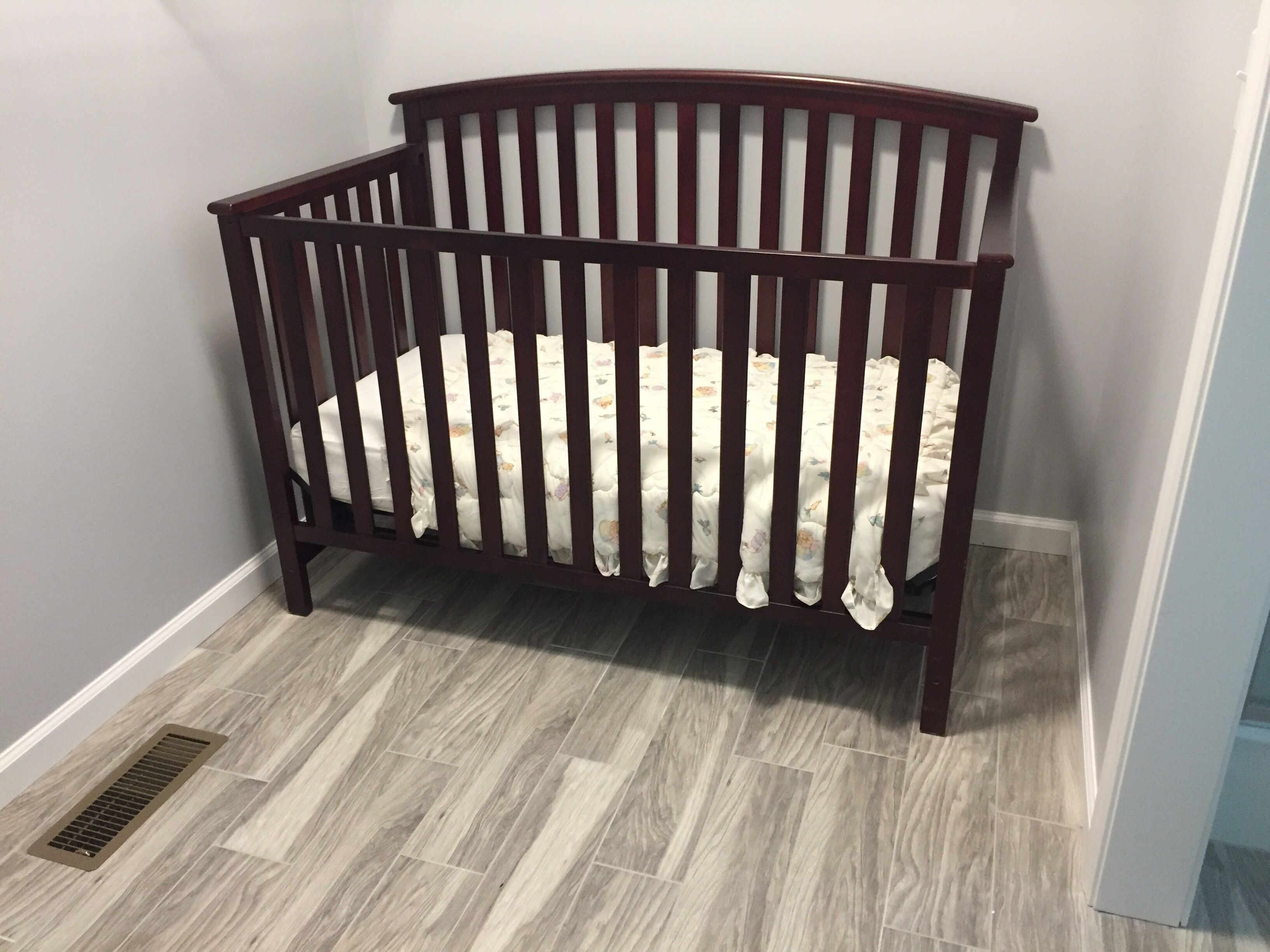 A wooden crib with a white mattress in a room with grey walls and grey flooring.