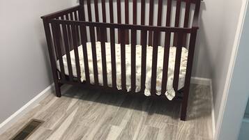 A wooden crib with a white mattress in a room with grey walls and grey flooring.