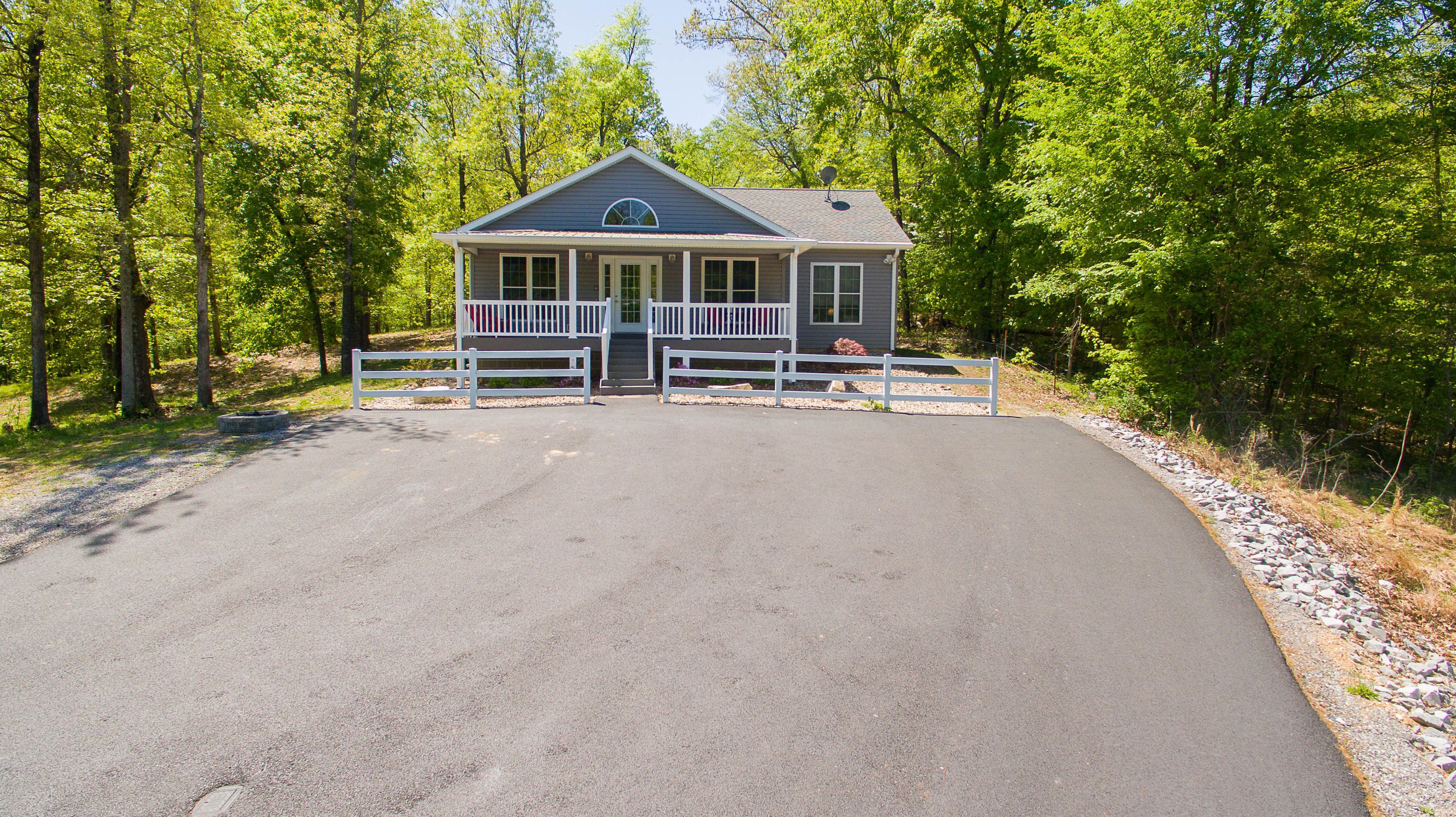 A single-story house with a porch, surrounded by a gravel driveway and a white fence.