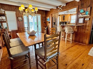 Un intérieur en bois comprenant une table à manger, des chaises, un lustre et un coin cuisine.