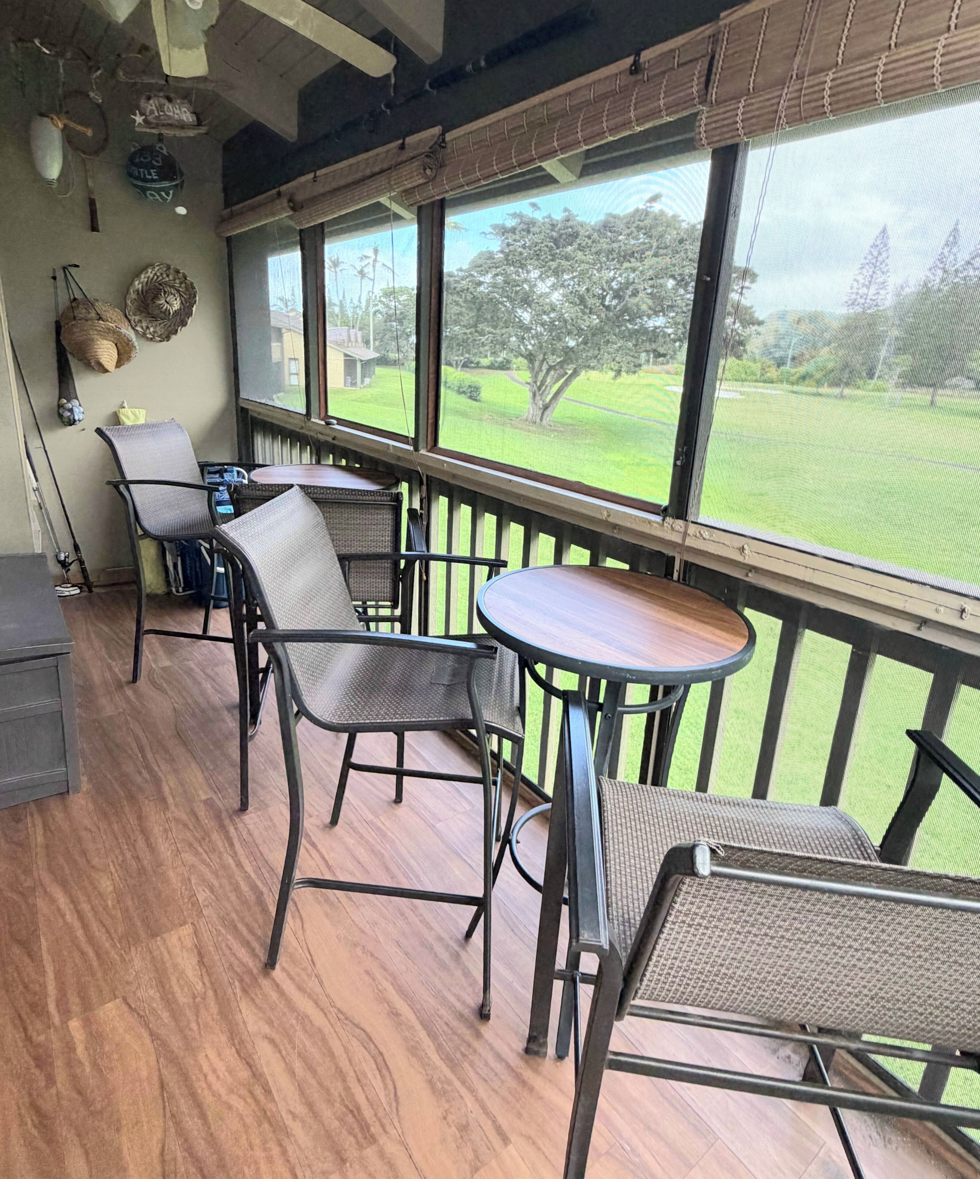 A covered patio with wicker furniture, a wooden table, and a view of a grassy area.
