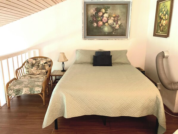Ein Schlafzimmer mit einem Bett, einem Sessel, einem Nachttisch und zwei Bildern an der Wand.
