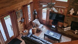A cozy cabin interior with a wooden ceiling, a fireplace, a sofa, a coffee table, and a TV.
