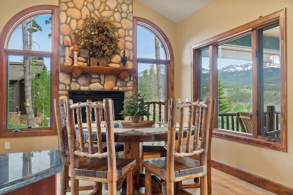 Un coin repas agrémenté d’une cheminée en pierre, de chaises en bois et de grandes fenêtres donnant sur une vue imprenable sur les montagnes.