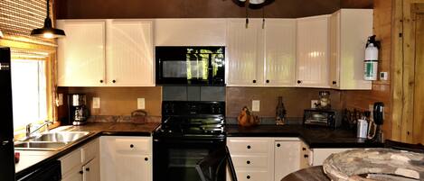 A kitchen with white cabinets, a black stove, and a wooden ceiling.