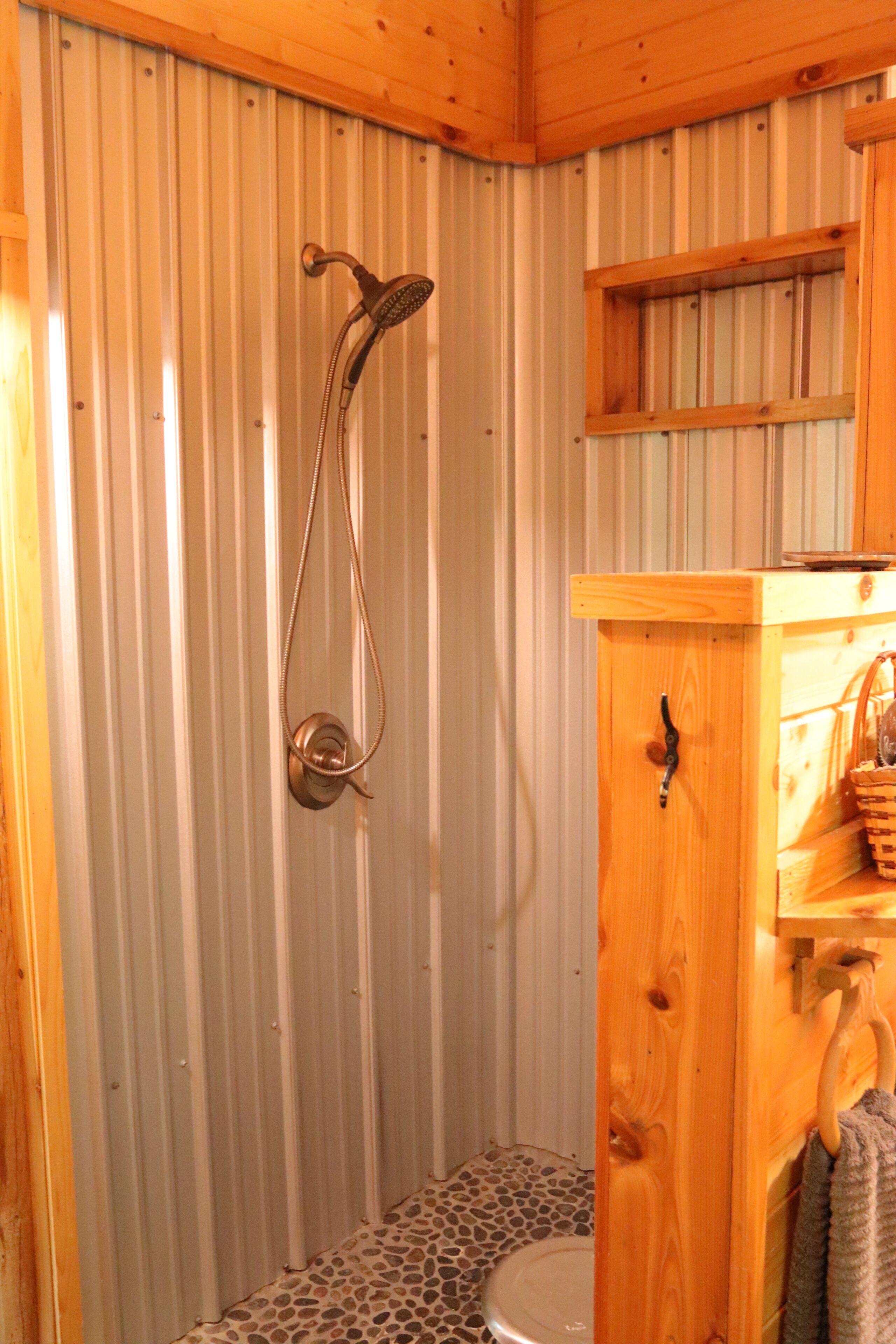 Ein Duschkabine aus Holz mit Duschkopf, Toilette und Holzschrank mit Handtuch an der Tür.
