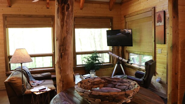 Een gezellig interieur van een blokhut, met houten lambrisering, een televisie op een statief, een comfortabele bank en een stenen schaal als middelpunt.
