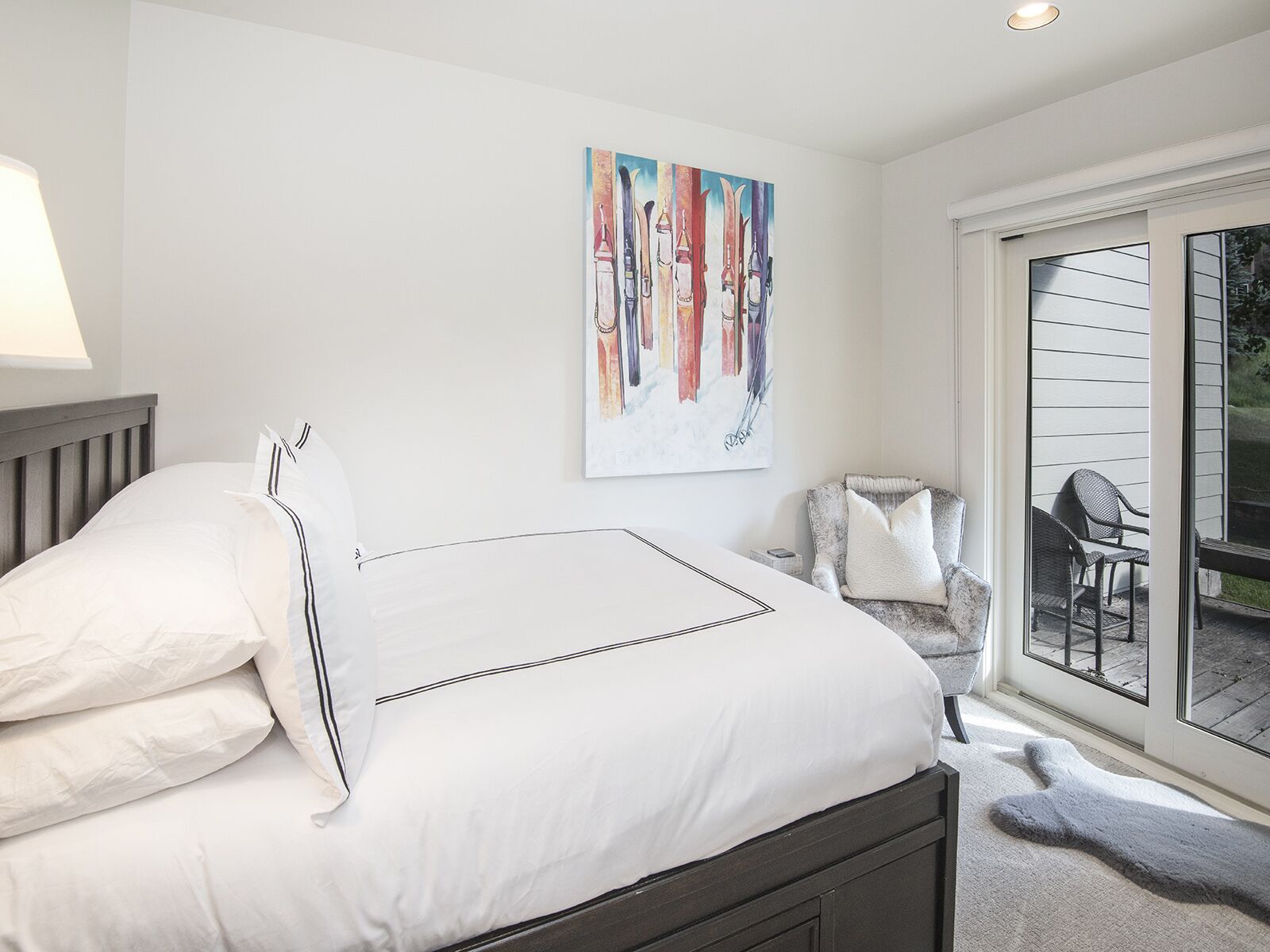 A bedroom with a bed, a painting, a chair, and a view of the outdoors.