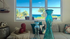 Una habitación con un amplio ventanal con vista a una playa, un modelo de velero y varios objetos decorativos.