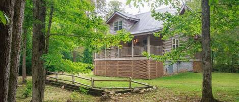 A log cabin with a deck and a wooden bridge in a forest setting.