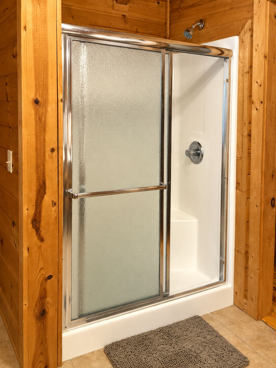 A shower enclosure with a glass door and a metal handle.