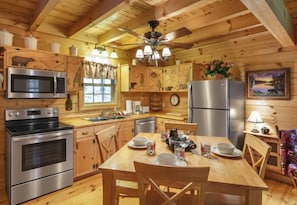 Een houten chalet van binnen met een keuken, eettafel, stoelen, een koelkast en een magnetron.