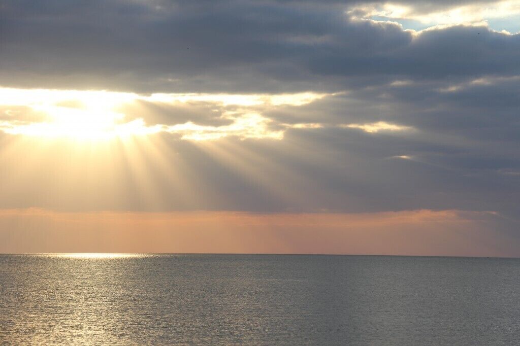 A sunset over a calm sea with sunlight streaming through clouds.