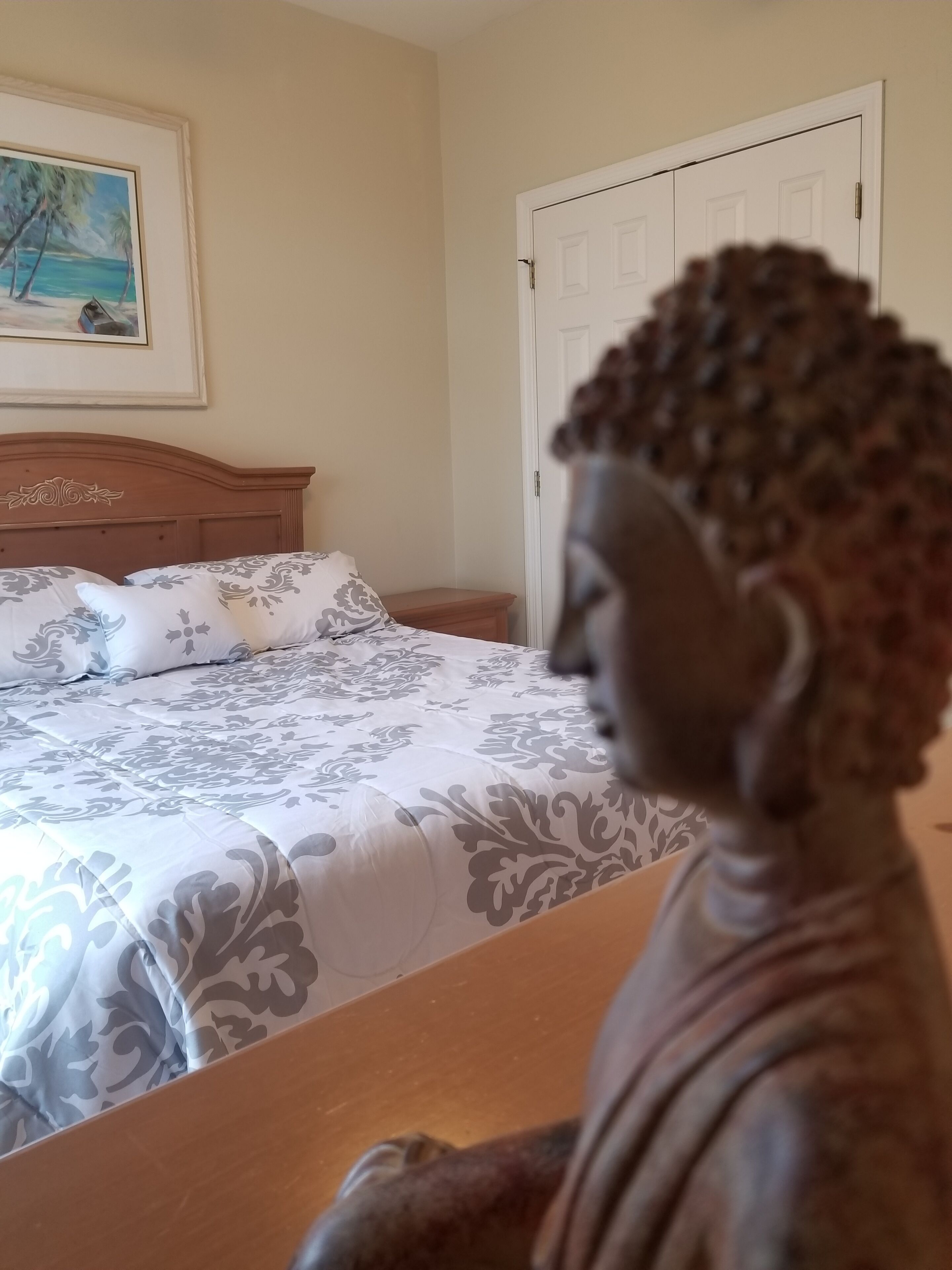 Un dormitorio con cama, mesita de noche, una puerta y un cuadro en la pared.