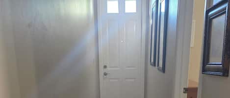 A hallway with a white door, tiled floor, and framed pictures on the walls.