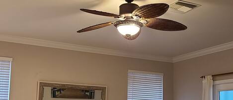 A living room with a sectional sofa, a coffee table, a ceiling fan, and a television on the wall.