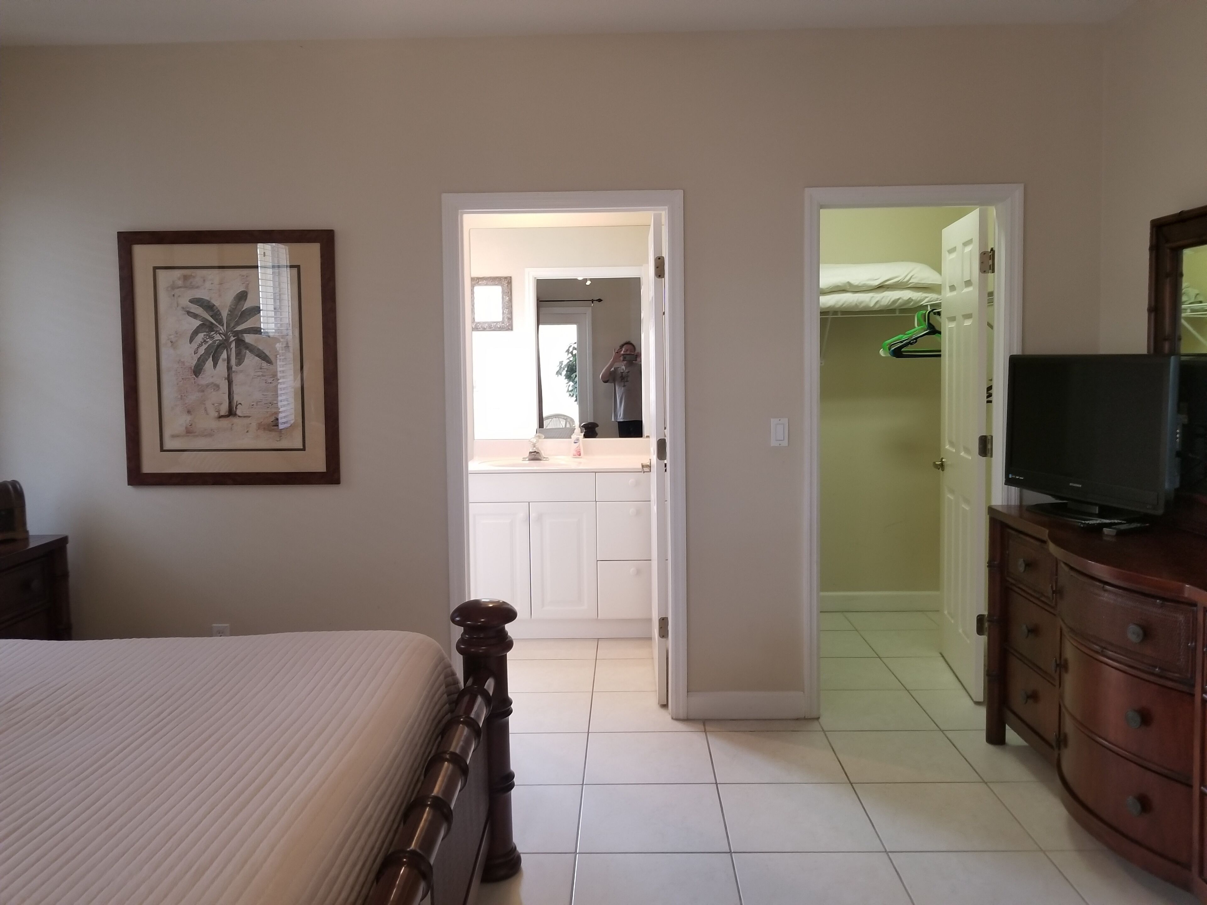 A bedroom with a bed, a dresser, a television, and a bathroom visible through an open door.
