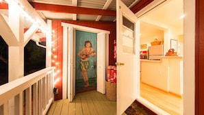 A wooden deck with a white railing, a door with a mural, and a kitchen area with a refrigerator and a basket.