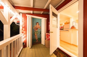 Eine Holzterrasse mit weißer Brüstung, eine Tür mit Wandgemälde und ein Küchenbereich mit Kühlschrank und Korb.