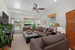 A spacious living room with a ceiling fan, a large window, and a view of the outdoors.