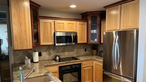 A kitchen with wooden cabinets, stainless steel appliances, a granite countertop, and a tiled backsplash. - Breathtaking Ocean View Penthouse with Spacious Patio, E-305  (Oceanside)
