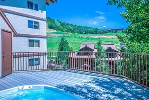 A deck with a hot tub, overlooking a green landscape and a bridge.