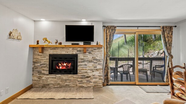 A living room with a fireplace, a flat-screen TV, and a sliding glass door leading to an outdoor deck. - Ski-In/Ski-Out 1-Bedroom Condo w/ Balcony and Fireplace! (Steamboat Springs)