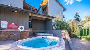 Zona de piscina con jacuzzi, paredes de piedra y cartel con las normas de la piscina.