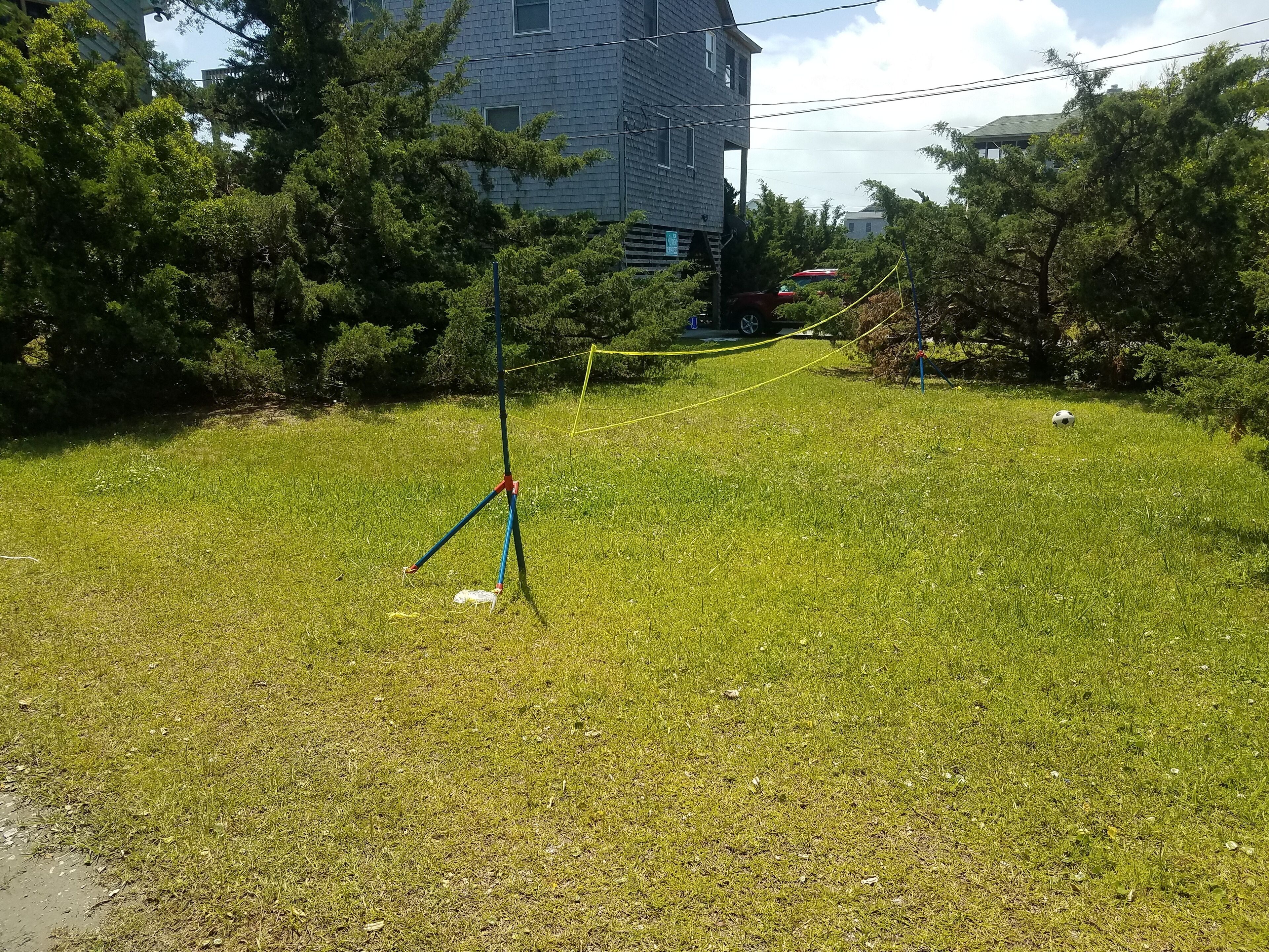 A grassy field with a tripod and a yellow rope, surrounded by trees and a building in the background.