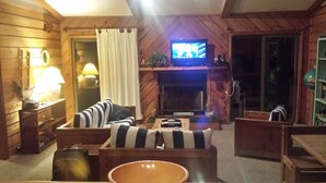 A cozy log cabin interior with a fireplace, a television, and a dining area. -  TOP DECK OCEAN VIEWS HOTTUB
 
 SHORT STROLL  BEHIND  HOUSE 
    TO SERENE BEACH (Salvo)