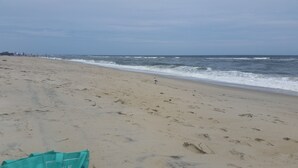 A wide sandy beach with footprints leading to the water, a clear sky, and a distant shoreline with people. -  TOP DECK OCEAN VIEWS HOTTUB
 
 SHORT STROLL  BEHIND  HOUSE 
    TO SERENE BEACH (Salvo)