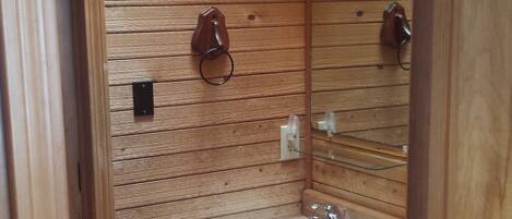 A wooden-paneled bathroom with a sink, mirror, and toilet.
