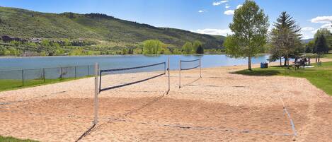 A sandy beach volleyball court with a net, a lake, and trees in the background.