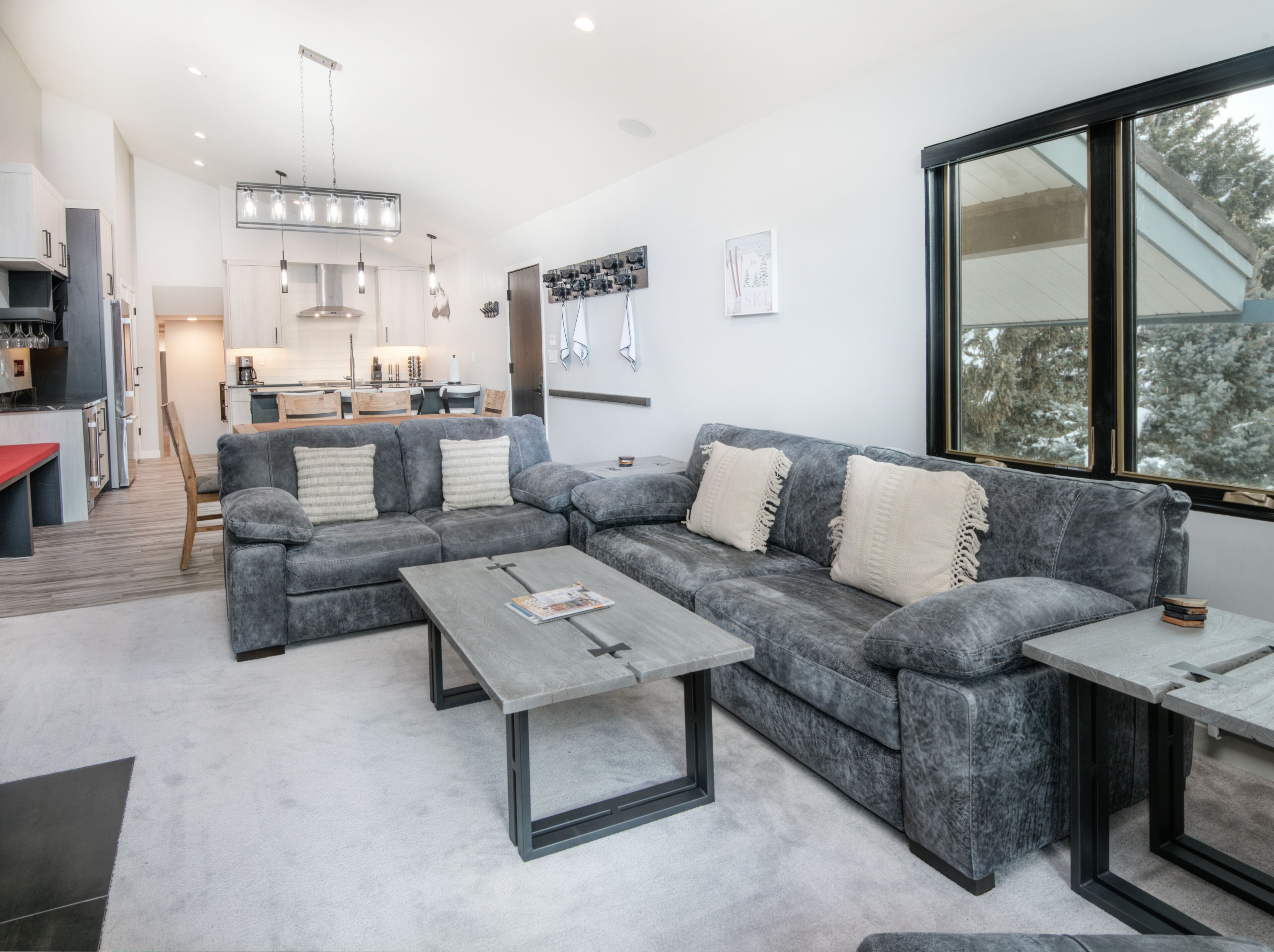 A modern living room with a grey sectional sofa, a coffee table, and a dining area in the background.