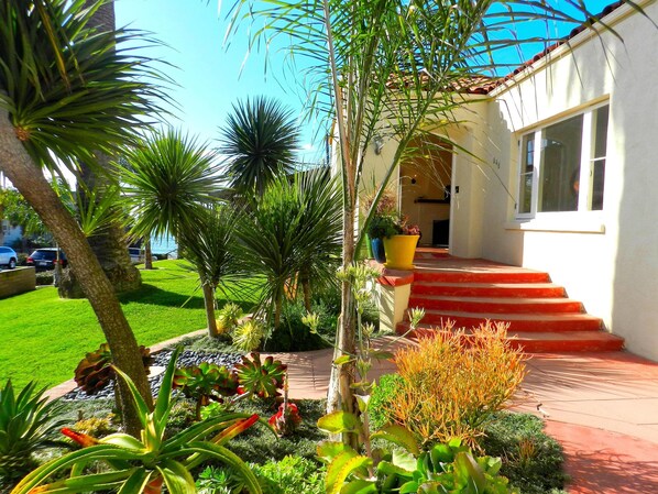 Un jardín bien cuidado con diversas plantas y una escalera roja que conduce a un edificio blanco.