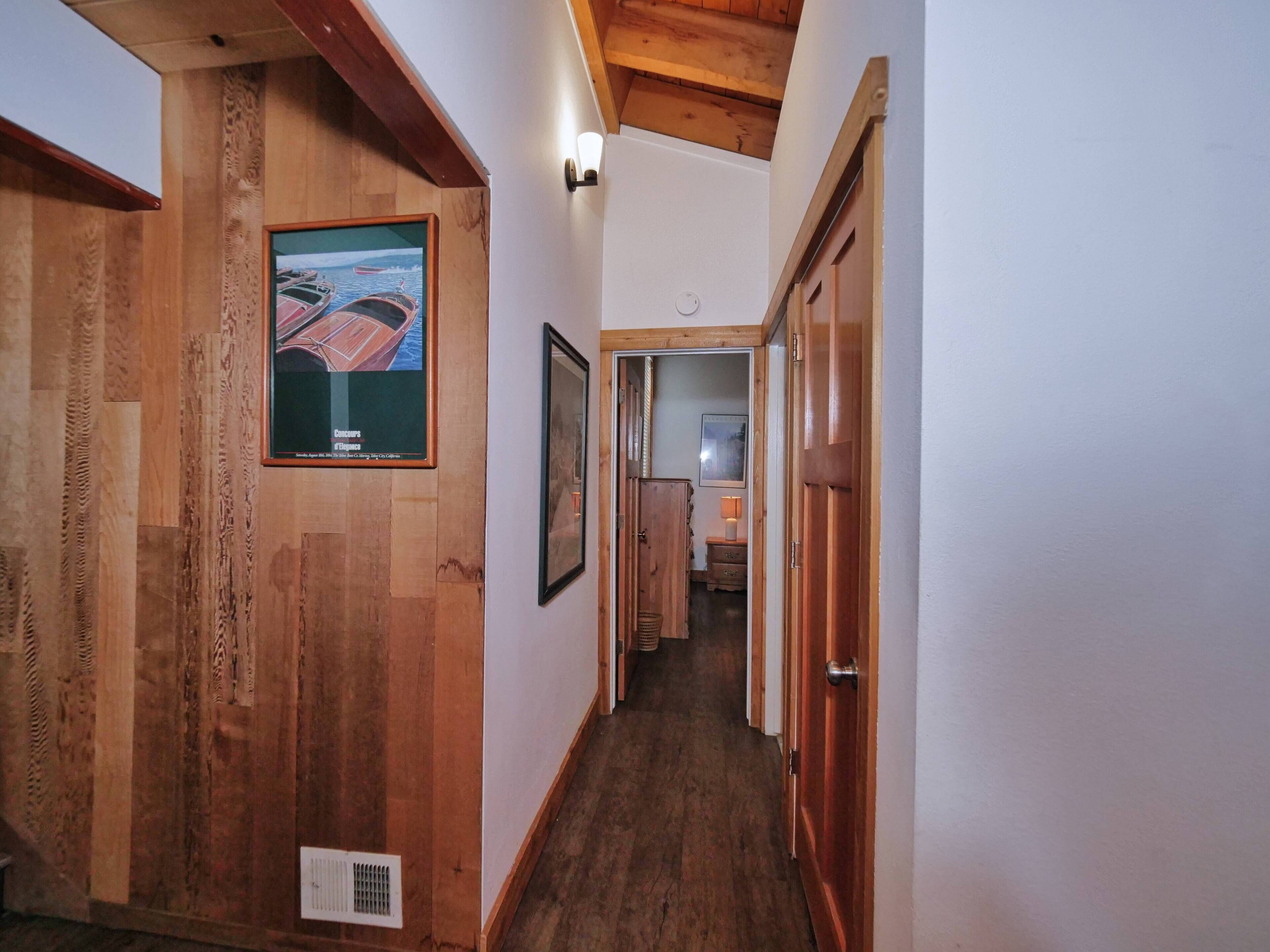 A wooden hallway with a framed picture of a boat, a vent, and a door leading to another room.
