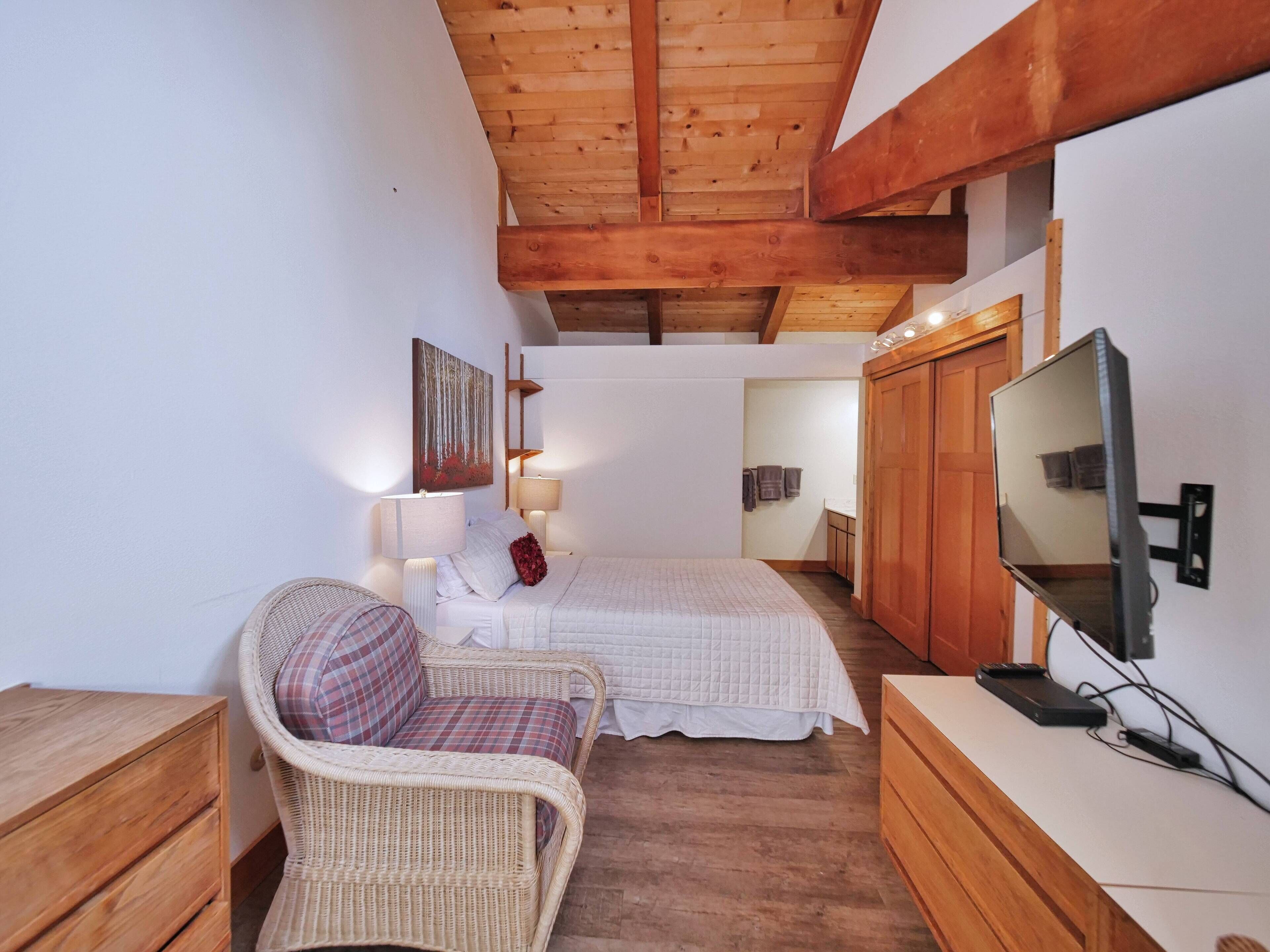 A bedroom with a bed, a chair, a TV, wooden furniture, and a painting on the wall.