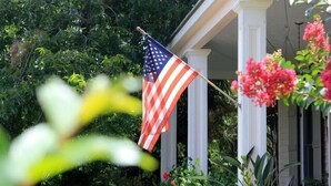 An American flag on a flagpole in front of a house with a porch. - Quaint Cottage, Walk to Beach and Old Town Bay St. Louis (Bay St Louis)