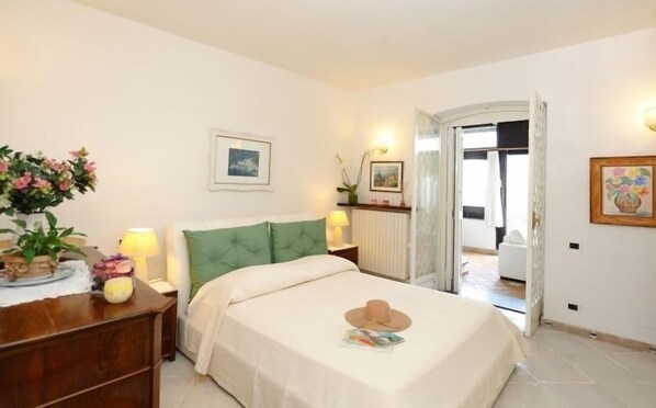 Une chambre à coucher comprenant un lit, des tables de chevet, une commode, un miroir et une porte donnant sur une autre pièce.